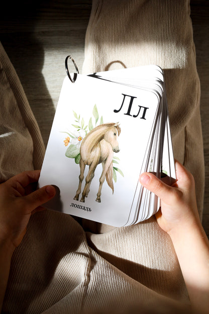 Child holding ring-bound cards showing a horse — Russian alphabet cards